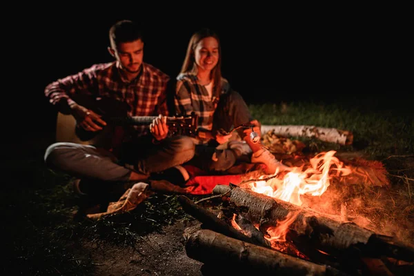 Young couple in love on romantic date on picnic at evening. Playing on guitar by the fire. Happy couple concept