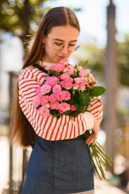 Bir demet taze pembe gül, genç ve güzel bir bayanın ellerinde.