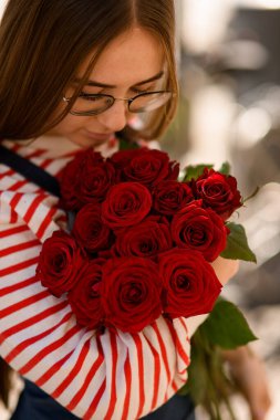 Genç bayanı nazikçe kucaklayan taze kırmızı gül buketinin yakın çekimi.