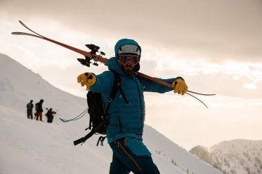 Kayak takımlı, sırtında gökyüzü, karla kaplı dağda sırt çantasıyla adamın yakın görüntüsü. Kayak turu