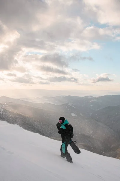 穿着滑雪服 手里拿着雪板的人 站在雪地覆盖的斜坡上 面对着美丽的冬季山景 — 图库照片
