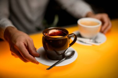 Bir erkeğin elinde kaşıkla çay fincanı ve limonlu çay tabağına odaklan.