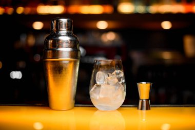 Çelik karıştırıcının yakın plan görüntüsü ve buzlu cam ve sarı masa yüzeyinde jigger.