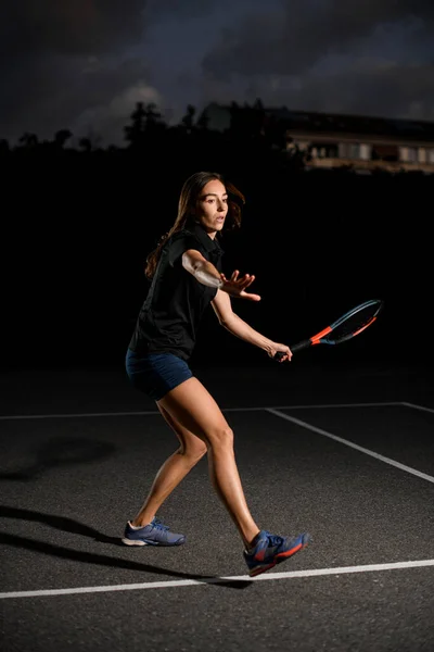 プロの大人の女子テニス選手で強い足で屋外テニスコートにラケットを手に 暗い背景 — ストック写真