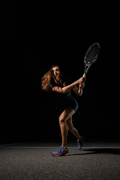 Great view of athletic woman tennis player with racket in special pose which preparing to playing tennis. Shot before to hitting tennis ball. Dark background
