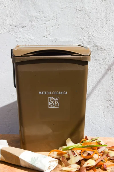 Image of a brown bin where you can throw away the organic rubbish next to the compostable bags and a lot of vegetable peels