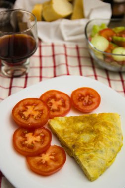 Bir porsiyon patates omleti ve domates dilimleri ile bir bardak şarap, ekmek ve salata.