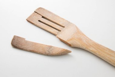 A close up of a used wooden spatula that has snapped at its weakest part on a neutral white background
