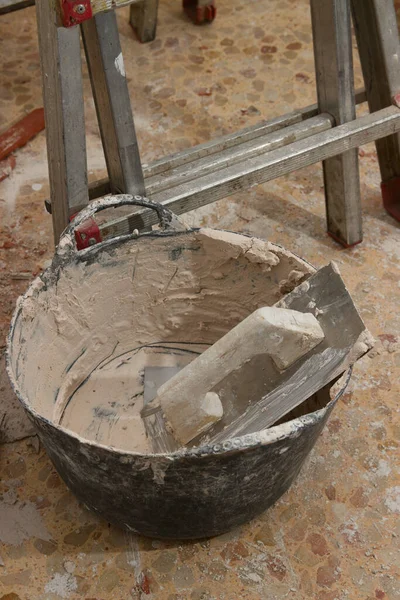 Close-up of the tools of a bricklayer who is repairing the interior of a house, we see a trowel, a carrycot with plaster and a ladder