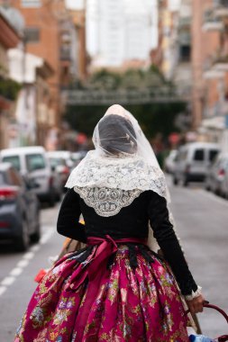 Fallera gibi giyinmiş bir kadının elinde küçük bir sepetle İspanya 'nın Valencia Fallas şehrinde adak adadığı bir kadının fotoğrafı.