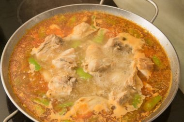 Ev yapımı seramik bir hobda kaynar suyla hazırlanan Valencia paella resmi.