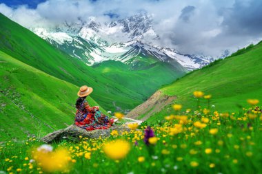Gürcistan 'ın Ushguli yakınlarındaki en yüksek Gürcü dağı Shkhara' ya karşı yeşil otlaktaki kayada oturan turist.
