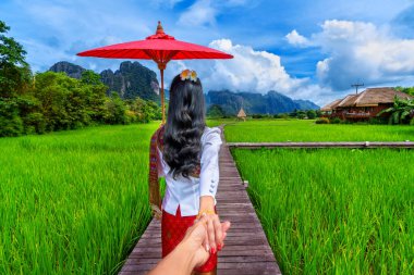 Women tourists holding man's hand and leading him to wooden path with green rice field in Vang Vieng, Laos.