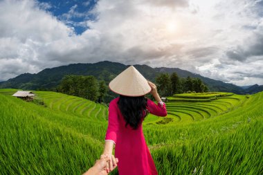 Vietnam kültürü giymiş Asyalı bir kadın geleneksel erkeğin elini tutuyor ve onu Mu Cang Chai, Yen Bai, Vietnam 'daki pirinç teraslarına götürüyor..