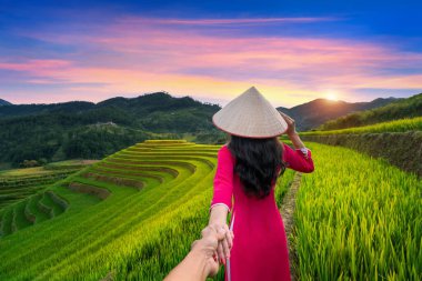 Vietnam kültürü giymiş Asyalı bir kadın geleneksel erkeğin elini tutuyor ve onu Mu Cang Chai, Yen Bai, Vietnam 'daki pirinç teraslarına götürüyor..