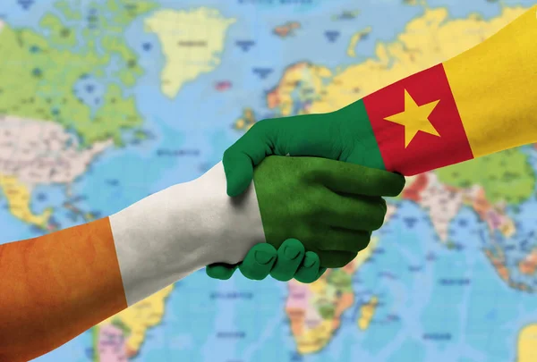 Handshake between Cameroon and Cte d\'Ivoire flags painted on hands With background of world map