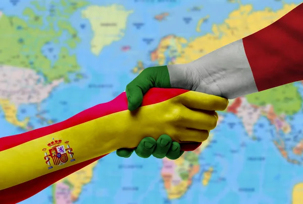 Handshake between Italy and Spain flags painted on hands.With background of world map