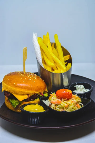 fast food menu. hamburger, french fries and salad. burger with beef stake, cheese and pickle. mayonnaise ketchup mustard on the  plate.