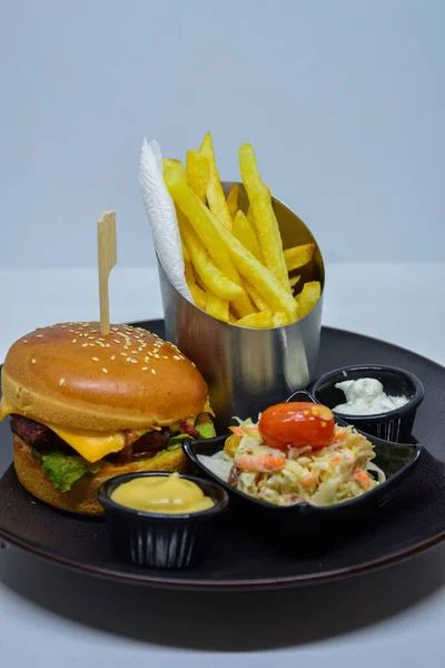 fast food menu. hamburger, french fries and salad. burger with beef stake, cheese and pickle. mayonnaise ketchup mustard on the  plate.