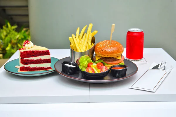 fast food menu. hamburger, french fries and salad. burger with beef stake, cheese onion and pickle. mayonnaise ketchup mustard on the white plate.