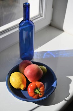 Pencerenin yanında mavi bir şişe, biber ve meyve ile sakin bir hayat.