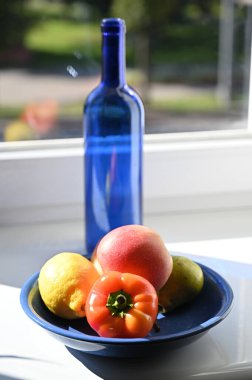 Pencerenin yanında mavi bir şişe, biber ve meyve ile sakin bir hayat.