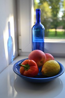 Pencerenin yanında mavi bir şişe, biber ve meyve ile sakin bir hayat.