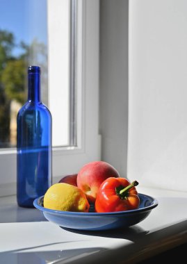 Pencerenin yanında mavi bir şişe, biber ve meyve ile sakin bir hayat.