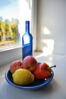 Pencerenin yanında mavi bir şişe, biber ve meyve ile sakin bir hayat.