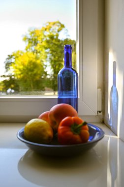 Pencerenin yanında mavi bir şişe, biber ve meyve ile sakin bir hayat.
