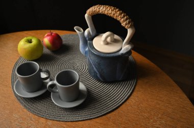 Masada olgun elma, bardak ve çaydanlık var. 