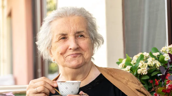 Old smiling woman drinking turkish coffee and relaxing on balcony. Senior woman in 70s smiling and enjoying the time.