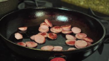 Dilimlenmiş sosisler kızartma tavasında kızartılır. Bir kadının eli kırmızı dolma biber ekler.