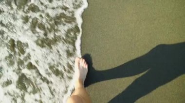 Yukarıdan yakından bakınca sahilde yürüyen, deniz dalgalarıyla yıkanan erkeklerin bacaklarını görüyoruz..