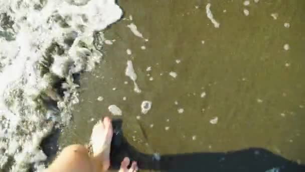 Närbild från ovan visar mäns ben gå längs stranden, tvättas av havsvåg. — Stockvideo