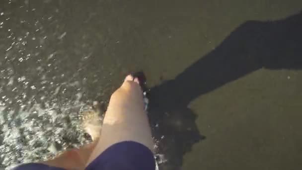 Close-up from above shows men's legs walking along beach, washed by sea wave. — Stock Video