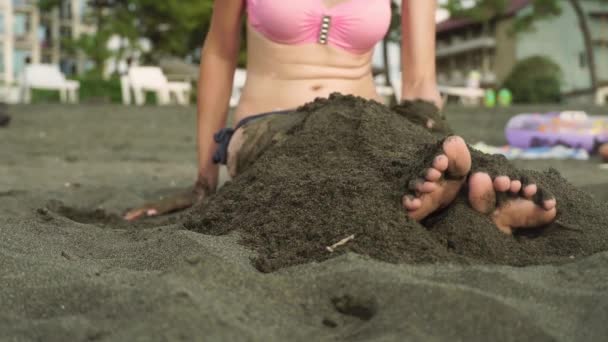 Жінка сидить на пляжі з чорними пісками і намагається поховати себе . — стокове відео