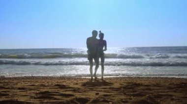 Genç, seksi bir çift, bir kadın ve bir erkek, deniz kıyısında dalgalarda zıplıyorlar..