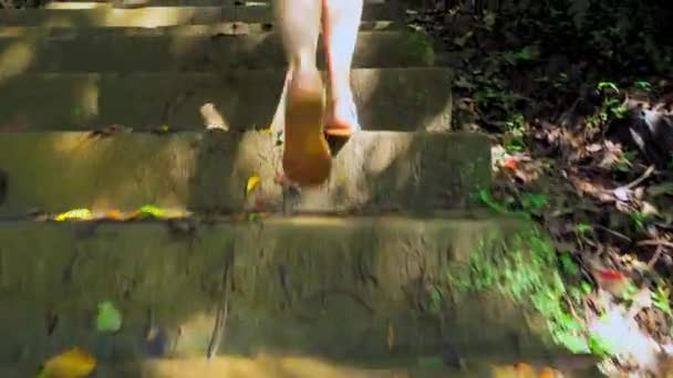 Een vrouw in sandalen beklimt een oude vervallen stenen trap. — Stockvideo