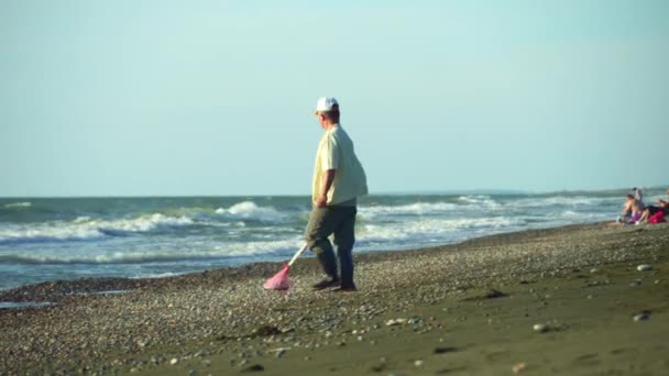 Ένας άντρας με ανιχνευτή μετάλλων στην παραλία κατά τη διάρκεια μιας καταιγίδας. ψάχνει για κοσμήματα. — Αρχείο Βίντεο