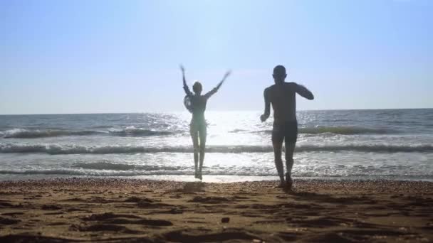 Młoda seksowna para, kobieta i mężczyzna skaczą na falach na brzegu morza. — Wideo stockowe
