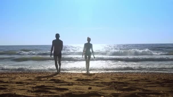 Giovane coppia sexy, donna e un uomo, saltando sulle onde sulla riva del mare. — Video Stock