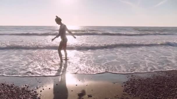 Mulher esbelta chuta a água do mar na praia de areia. Salpicos de água — Vídeo de Stock
