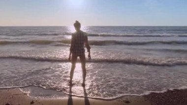 İnce bir kadın ellerini kaldırıp kumsalda ellerini çırpıyor..