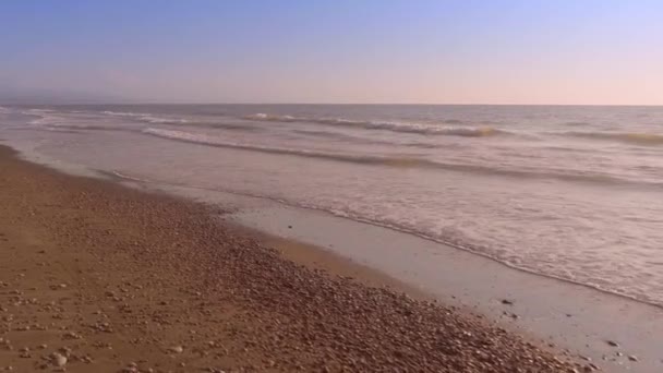 Tengeri hullámok közelsége, amint lábnyomokat mosnak le a homokos parton.. — Stock videók