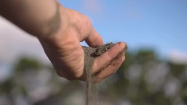 Рука крупным планом хватает горсть сухого песка и позволяет ему упасть между пальцами. — стоковое видео