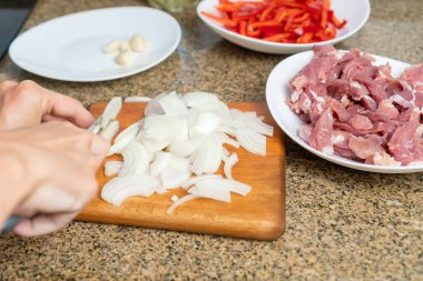 Kadınların ellerinin, mutfaktaki bir kesme tahtasının üzerinde beyaz soğan keserken yakın plan, yanında da domuz eti ve tatlı kırmızı biber parçaları var.