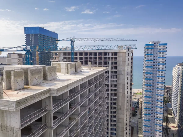 Close-up view from a drone on the construction of a multi-storey building in summer against the background of the sea