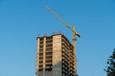 Sarı bir vinç ve çok katlı bir binanın mavi gökyüzü arka planına yakın çekim.