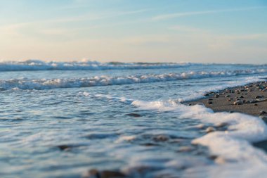 Kumsalda kumlu bir plaja yuvarlanan köpüklü deniz dalgalarının yakın çekimi..